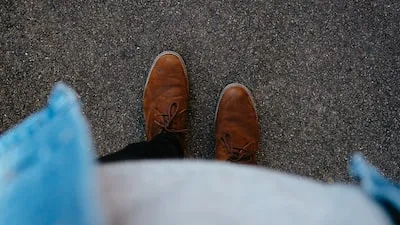 person wearing pair of brown leather boots standing on asphalt surface