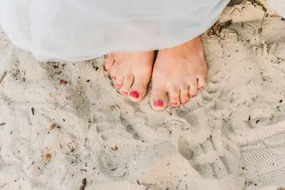 person with red pedicure standing on white textile