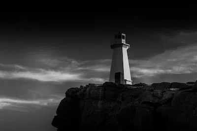 grayscale photo of lighthouse on rock formation